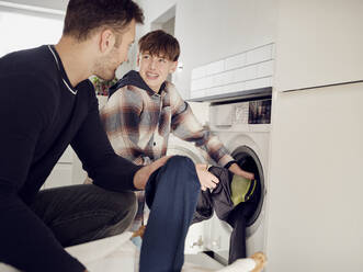 Father and son putting laundry into washing machine at home - PWF00409