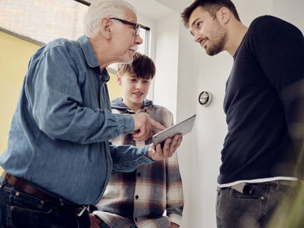 Sohn, Vater und Großvater sehen sich die Steuerung des intelligenten Thermostats auf einem digitalen Tablet zu Hause an - PWF00414