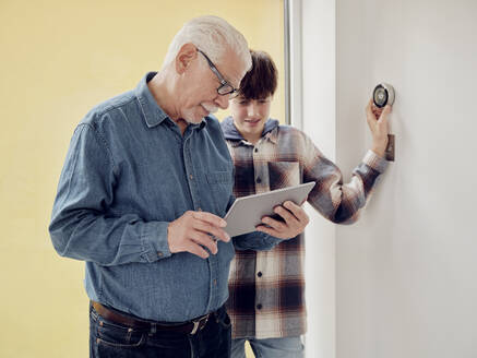 Grandfather and grandson looking at smart thermostat control on digital tablet at home - PWF00415