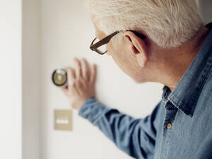 Ein älterer Mann stellt den intelligenten Thermostat an der Wand zu Hause ein - PWF00416