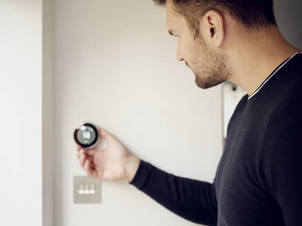 Mann beim Einstellen des intelligenten Thermostats an der Wand zu Hause - PWF00417