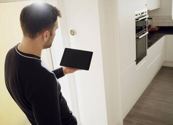 Mann hält digitales Tablet in der Küche zu Hause - PWF00422