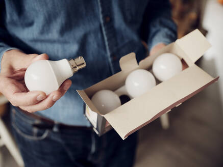 Close-up of man holding a box of LED lightbulbs - PWF00425