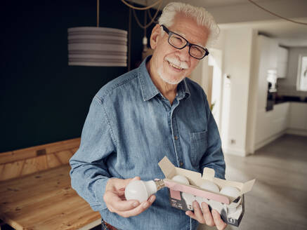 Ein älterer Mann hält eine Schachtel mit LED-Glühbirnen in der Hand - PWF00426