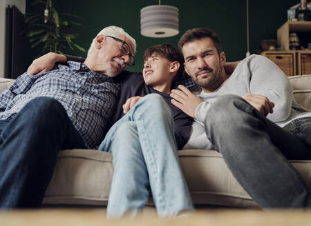 Großvater, Vater und Sohn sitzen zusammen auf der Couch im Wohnzimmer - PWF00428