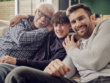 Glücklicher Großvater, Vater und Sohn sitzen zusammen auf der Couch im Wohnzimmer - PWF00429