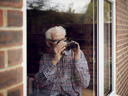 Älterer Mann schaut zu Hause mit einem Fernglas aus dem Fenster - PWF00441