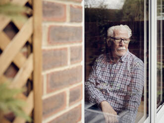 Pensive senior man looking out of the window at home - PWF00442