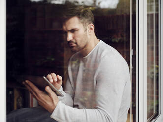 Man by the window at home using digital tablet - PWF00446