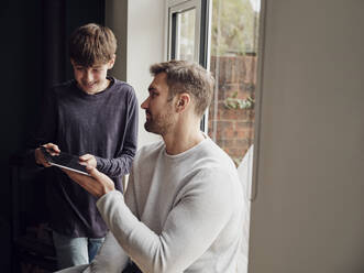 Vater und Sohn am Fenster zu Hause mit digitalem Tablet - PWF00448
