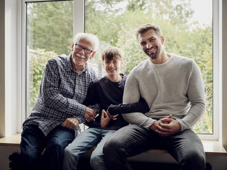 Glücklicher Großvater, Vater und Sohn sitzen zu Hause am Fenster - PWF00449