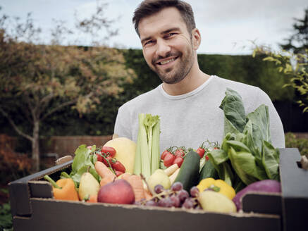 Lächelnder Mann trägt eine Kiste mit frischem Gemüse im Garten - PWF00453
