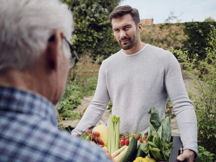 Mann liefert eine Kiste mit frischem Gemüse an einen älteren Mann im Garten - PWF00455