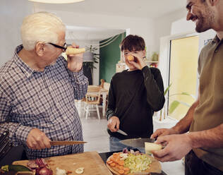 Großvater, Vater und Sohn schnippeln gemeinsam in der Küche Gemüse und haben Spaß mit Karotten - PWF00459