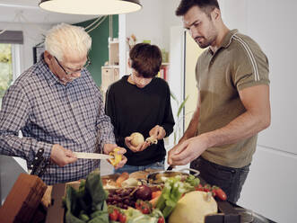 Grandfather, father and son preparing healthy meal in the kitchen together - PWF00462