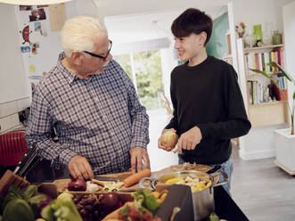 Grandfather and grandson preparing healthy meal in the kitchen together - PWF00463