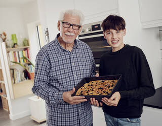 Porträt von Großvater und Enkel mit einem Backblech mit frischem Focaccia-Brot in der Küche - PWF00464