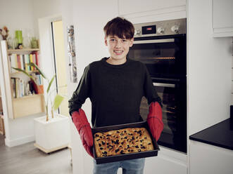 Porträt eines Jungen, der ein Backblech mit frischem Focaccia-Brot in der Küche hält - PWF00465