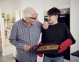 Großvater und Enkel halten ein Backblech mit frischem Focaccia-Brot in der Küche - PWF00466