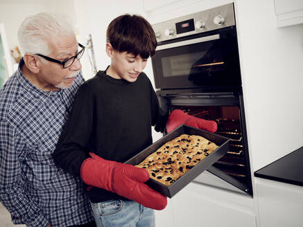 Großvater und Enkel halten ein Backblech mit frischem Focaccia-Brot in der Küche - PWF00467