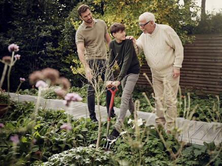 Vater und Großvater beobachten einen Teenager beim Graben im Garten - PWF00472