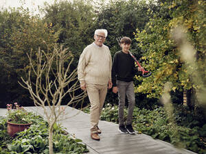 Großvater und Enkel gehen im Garten Junge trägt Gartengabel - PWF00473
