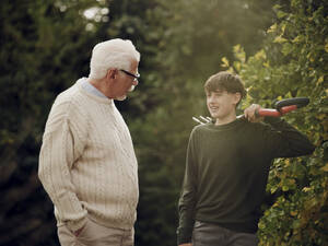 Großvater und Enkel unterhalten sich im Garten Junge trägt Gartengabel - PWF00475