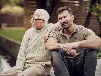 Adult son sitting with father in garden - PWF00490