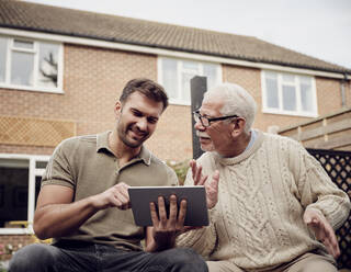 Vater und Sohn sitzen im Garten und benutzen ein digitales Tablet - PWF00496