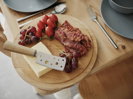 Cheese with tomatoes and grapes and bacon on kitchen table - PWF00499