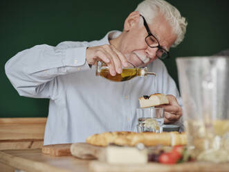 Älterer Mann beim Mittagessen, der Olivenöl in Focaccia träufelt - PWF00500