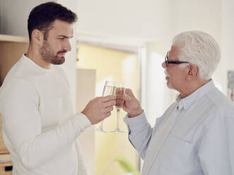 Älterer Mann und erwachsener Sohn feiern zu Hause und stoßen mit Champagner an - PWF00505