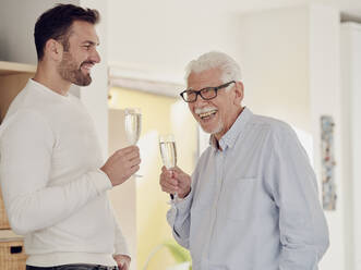 Älterer Mann und erwachsener Sohn feiern zu Hause und stoßen mit Champagner an - PWF00506