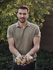 Mann steht im Garten und hält frisch geerntete Kartoffeln - PWF00508