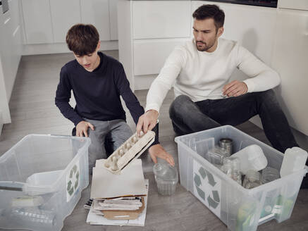 Father and son separating waste into recycling boxes - PWF00516