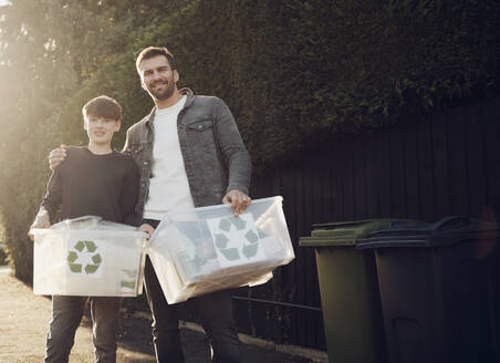 Vater und Sohn stehen im Freien und tragen Recycling-Kisten mit getrenntem Abfall - PWF00542