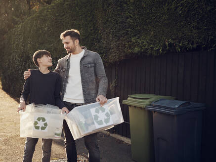 Vater und Sohn stehen im Freien und tragen Recycling-Kisten mit getrenntem Abfall - PWF00543