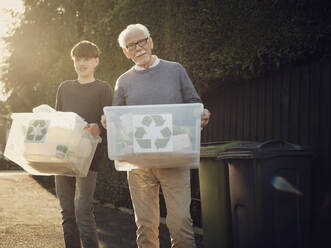 Großvater und Sohn stehen im Freien und tragen Recycling-Kisten mit getrenntem Abfall - PWF00544