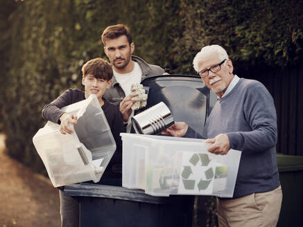 Großvater, Vater und Sohn stehen an einem Abfalleimer mit Recyclingboxen mit getrenntem Abfall - PWF00547