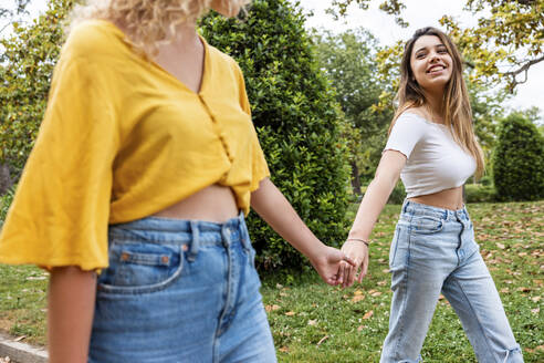 Lächelnde Frau hält die Hand eines Freundes beim Spaziergang im Park - WPEF06878