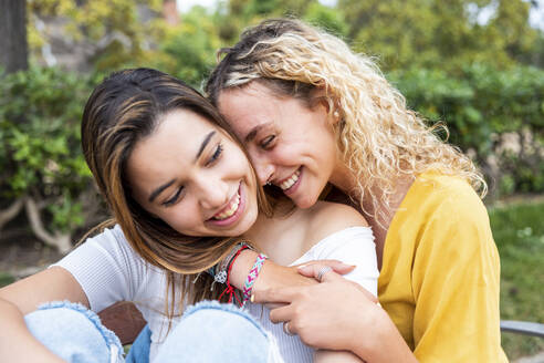 Lächelnde junge Frau mit blondem Haar, die ihre Freundin im Park umarmt - WPEF06899