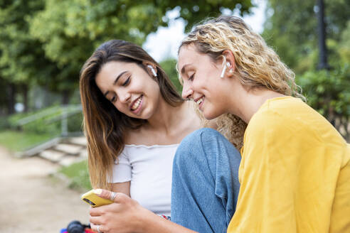 Lächelnde Frau, die ihr Mobiltelefon mit einem Freund im Park teilt - WPEF06901