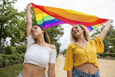 Lesbian couple holding rainbow flag in park - WPEF06902