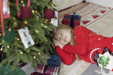 Lächelndes Mädchen entspannt sich unter dem Weihnachtsbaum auf dem Teppich zu Hause - ONAF00360