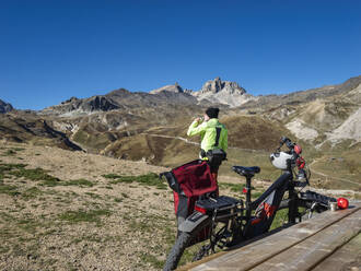 Senior man drinking water in front of mountain bike at Vanoise National Park, France - LAF02805