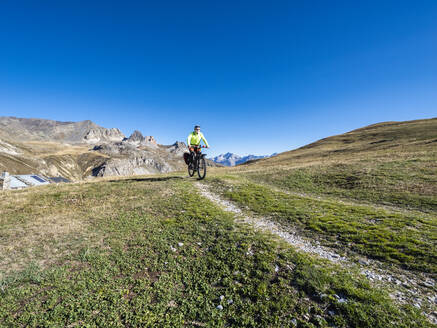 Senior man riding mountain bike on trail under blue sky, Vanoise National Park, France - LAF02810