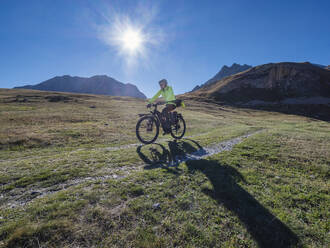 Älterer Mann fährt Mountainbike an einem sonnigen Tag unter blauem Himmel, Vanoise National Park, Frankreich - LAF02812