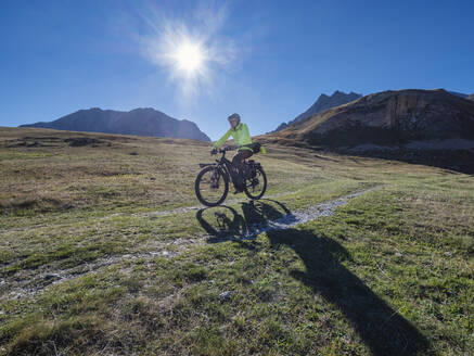 Senior man riding mountain bike on sunny day under blue sky, Vanoise National Park, France - LAF02812