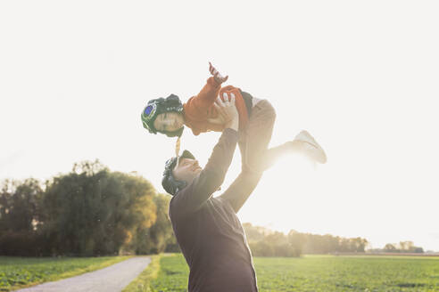 Mann hebt Sohn mit Flugbrille im Herbst hoch - AANF00421