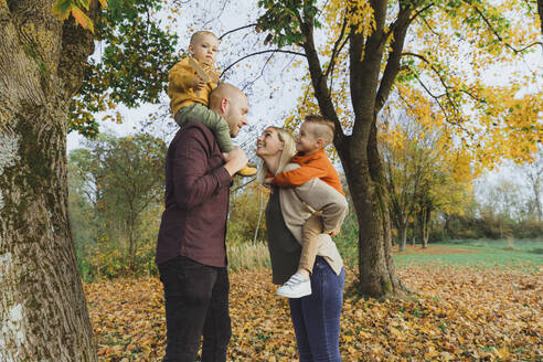 Lächelnde Frau, die ihren Sohn huckepack nimmt, und Mann, der den Jungen auf den Schultern trägt, im Herbstwald - AANF00424